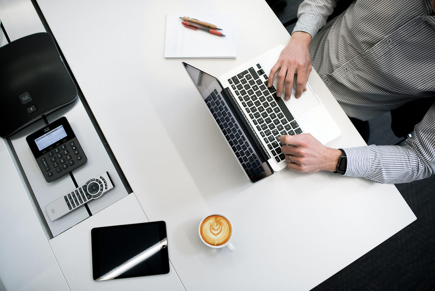 contract-management-for-doxa Article Banner Image - A photo of an employee taken from above showing his desk with laptop, coffee and office supplies