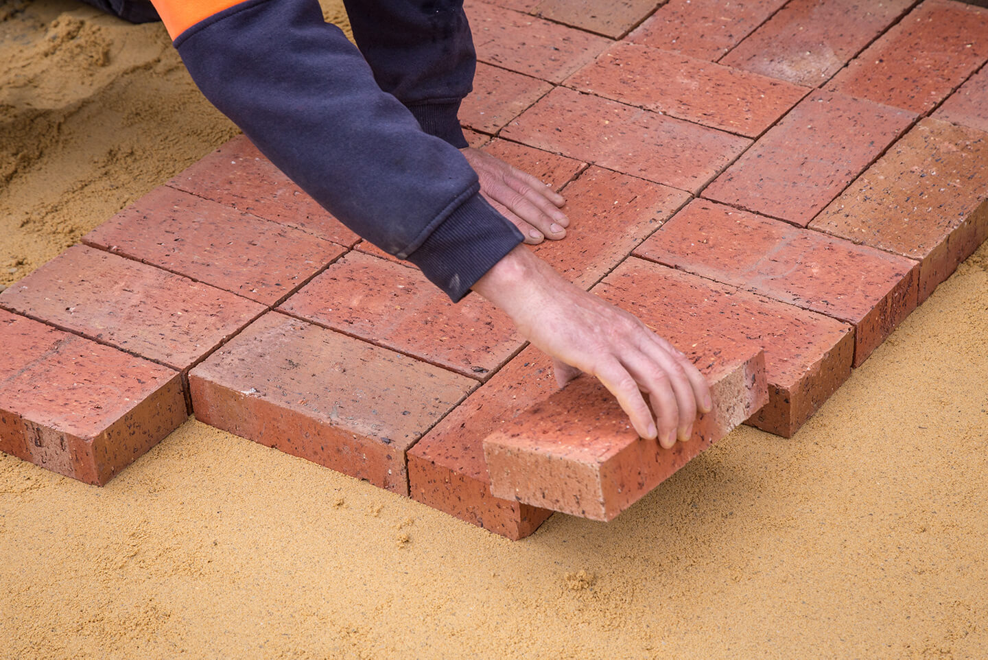 60f6a9b5ce5dee61c4aa736e_nwo_banner Article Banner Image - A photo of a hand placing a brick on the ground
